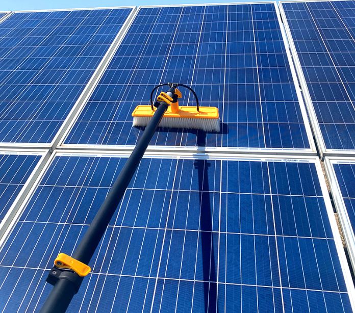Technician using a soft-bristle brush to clean a residential solar panel array